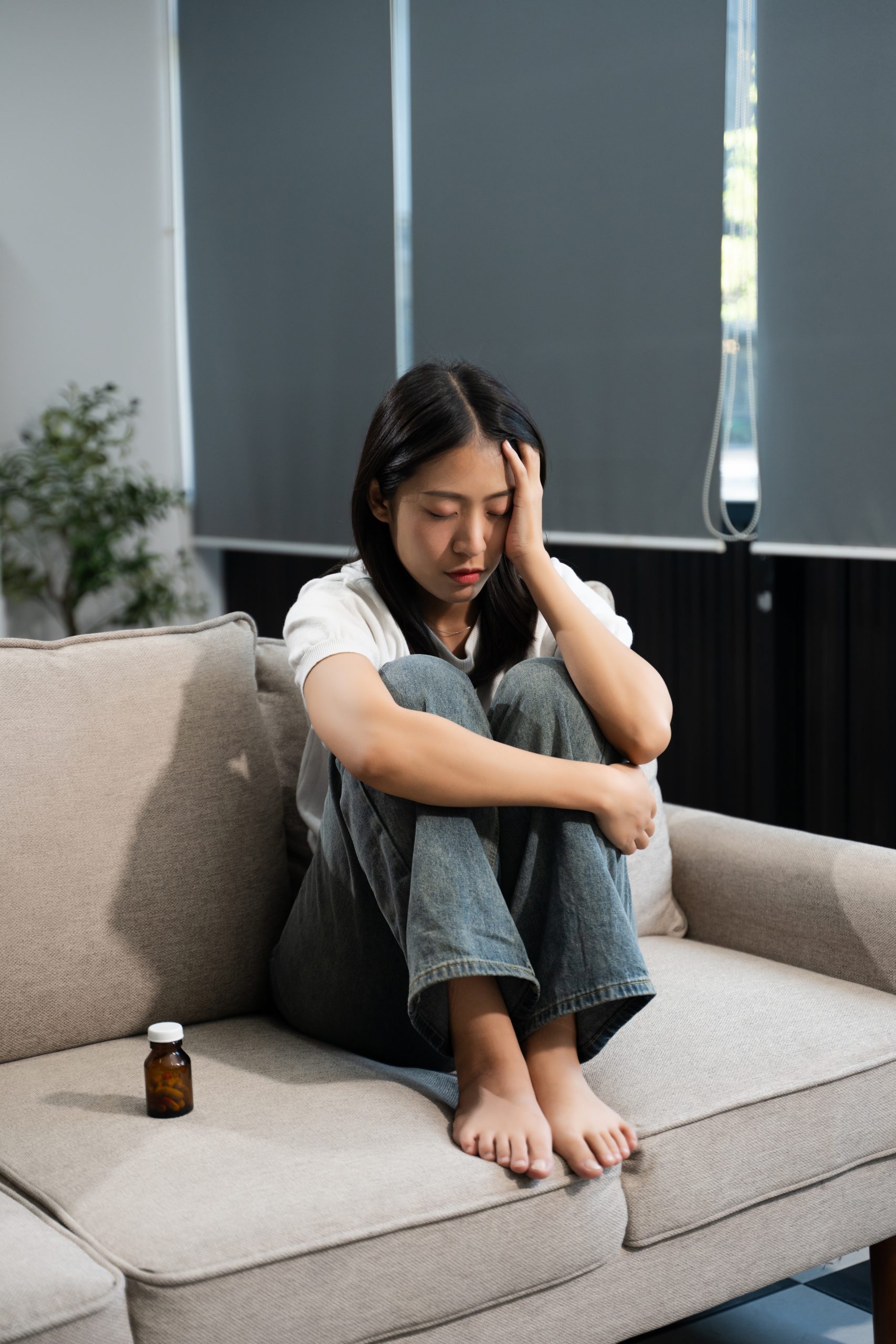 Pensive woman sitting on a sofa holding a medication bottle while reflecting on her mental health treatment and wellness