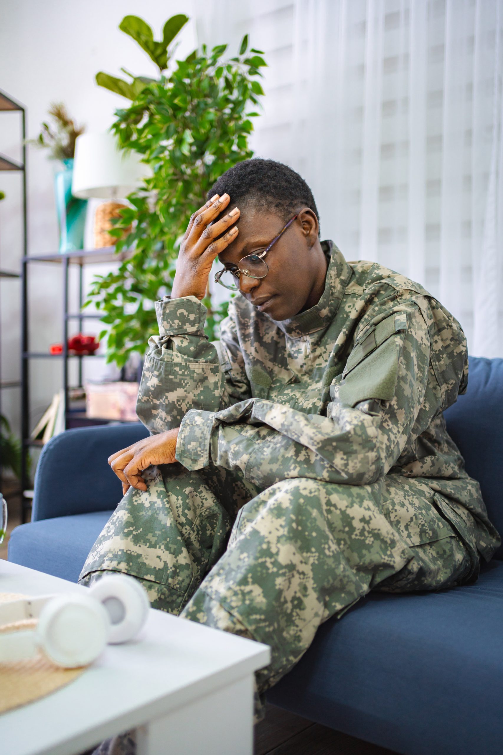 Worried service member wearing a camouflage uniform while sitting on a couch and experiencing emotional stress or anxiety