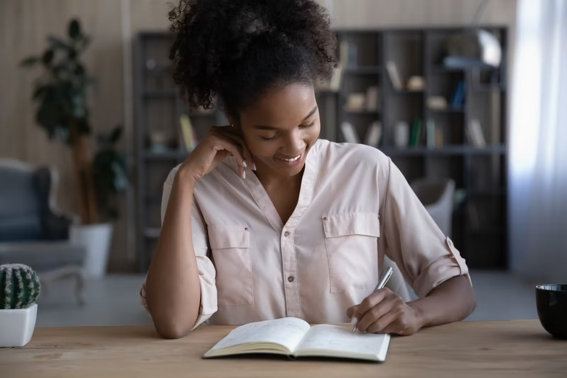 Smiling woman writing in a journal while reflecting on personal experiences and emotional wellness during a quiet moment